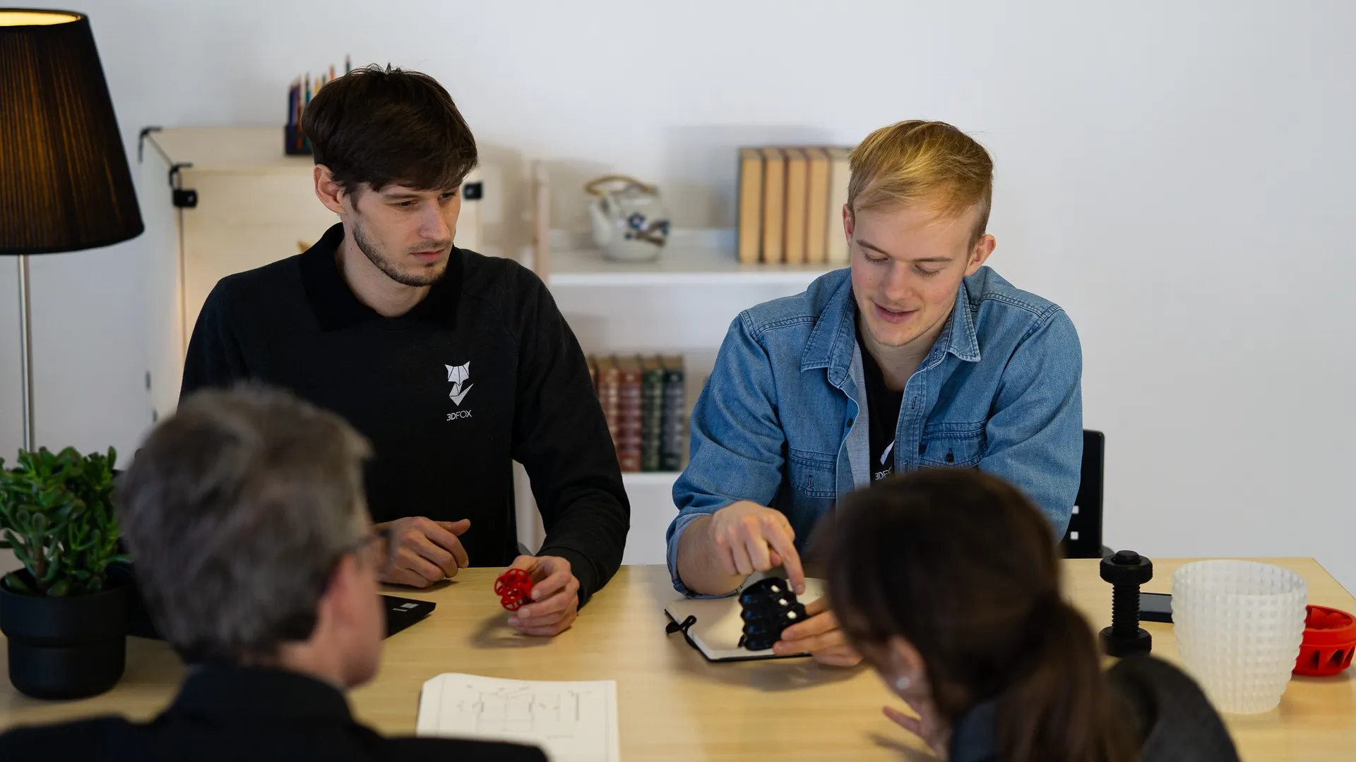 Foto von vier Personen gegenueber am Tisch sprechen ueber 3D Druck Teile