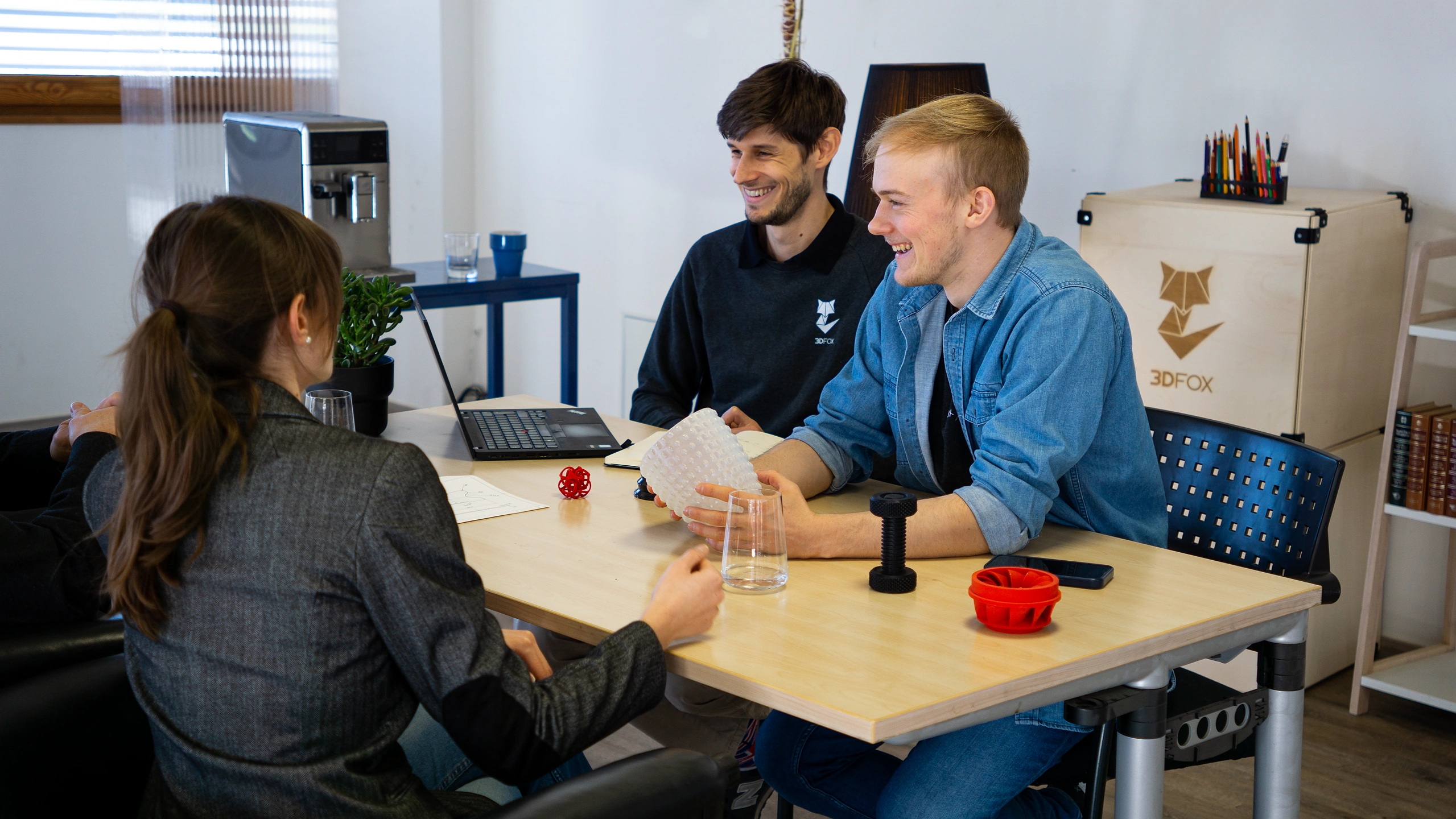 Vier Personen sitzen an einem Tisch gegenüber und führen ein Gespräch über 3D-Drucktechnologien